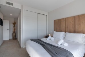 Moderni hotellihuone, jossa on suuri sänky, puinen pääty, yöpöytä lampun kanssa ja suuri maljakko, jossa on kuivattuja kasveja.