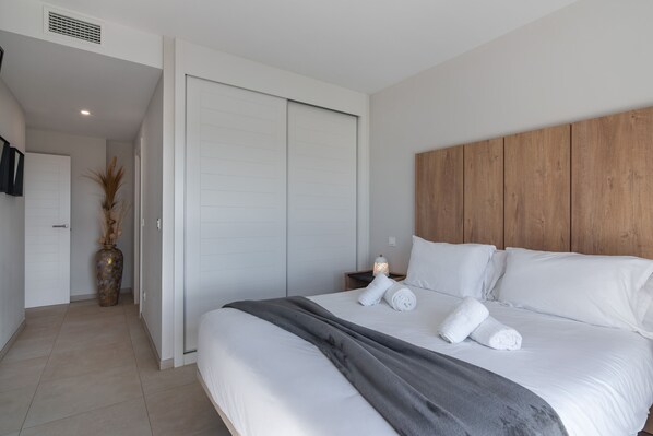 Een moderne hotelkamer met een groot bed, een houten hoofdbord, een nachtkastje met een lamp, en een grote vaas met gedroogde planten.