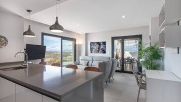 Uma cozinha moderna com uma ilha grande, uma área de jantar com vista e uma sala de estar com sofá e obras de arte.