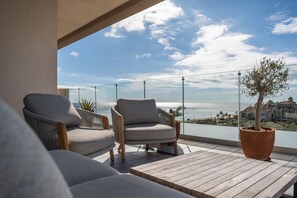 Een balkon met twee grijze fauteuils, een houten tafel en een plant in pot.
