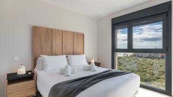 Quarto moderno com uma cama grande, cabeceira de madeira e vista para a cidade através de uma janela ampla.
