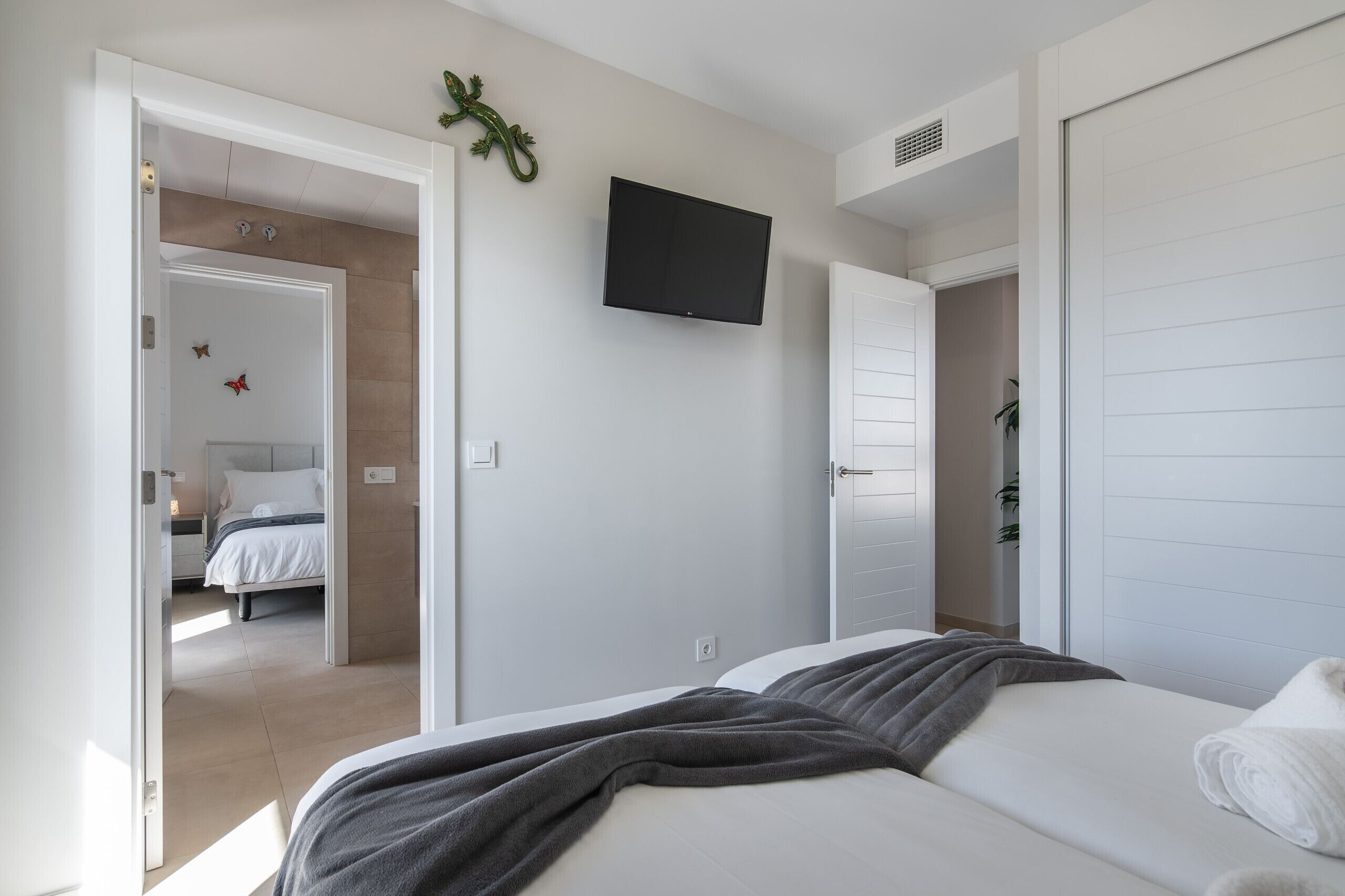 Une chambre à coucher moderne avec un lit, un téléviseur fixé au mur et une armoire.