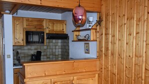 Une cuisine compacte dotée de meubles en bois, d’un four à micro-ondes, d’une machine à café et d’un luminaire suspendu.
