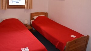 Une chambre avec deux lits simples, une fenêtre avec des rideaux, une petite table de chevet avec une lampe et un tableau au mur.