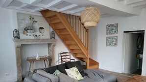 Una sala de estar con un sofá gris, una escalera de madera, un colgante de luz y una chimenea.