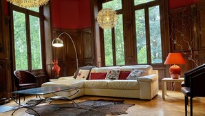 A cozy living room with a sectional sofa, a glass coffee table, a leather rug, and large windows with natural light. - Château de la Coudraie Sarthe 72560 (Changé)
