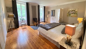 A spacious bedroom with a large bed, a sitting area with chairs, a floor lamp, and a painting on the wall. - Château de la Coudraie Sarthe 72560 (Changé)