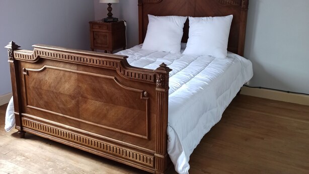 Un letto di legno con testiera, un comodino con una lampada e un pavimento in legno.