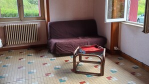 Una stanza con un divano viola, una sedia di legno, un termosifone e un pavimento piastrellato con motivo geometrico.