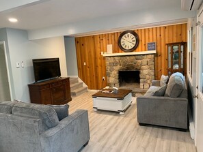 A living room with a stone fireplace, a clock, a television, and a sofa.