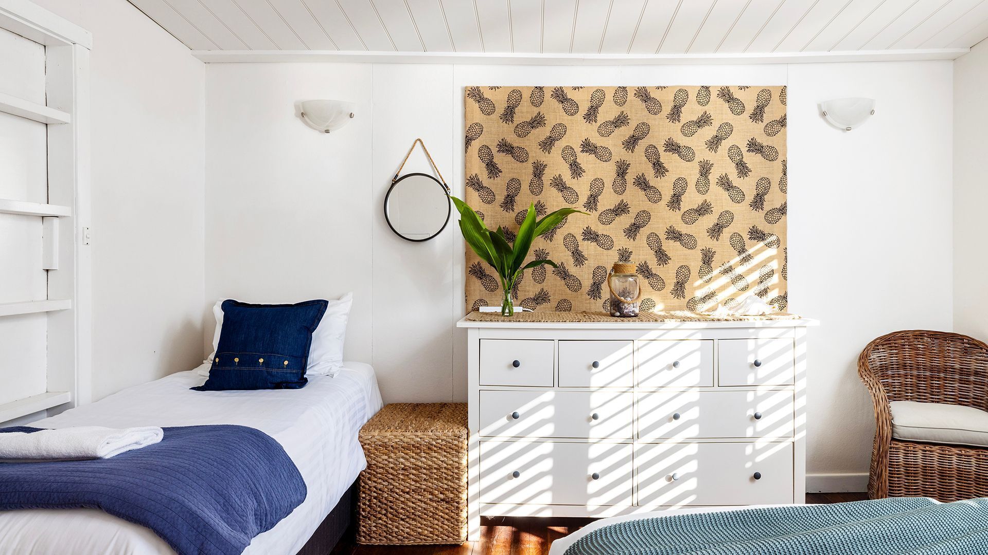 Ein Schlafzimmer mit einem Bett, einem Schminktisch, einem Korbstuhl und einer Wand mit Ananas-Muster.