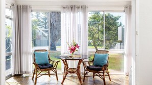 A sunlit room with a glass door, two wicker chairs with cushions, a small round table, and a vase with flowers. - Beach Bungalow – pet friendly beach house opposite dog beach (Corlette)