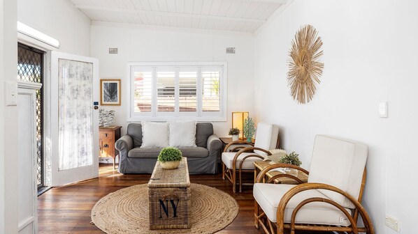 A spacious living room with a grey sofa, a round coffee table, and wicker chairs.