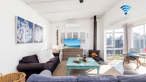 Een woonkamer met een bank, een salontafel, een open haard, een televisietoestel en een groot raam.