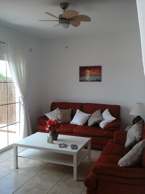 A living room with a red sofa, a white coffee table, and a ceiling fan.