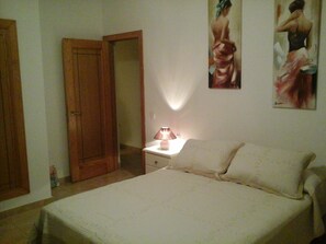 A bedroom with a bed, a nightstand, a lamp, and two paintings on the wall.