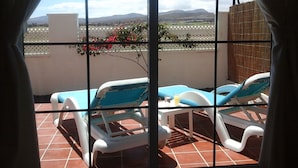 Un balcón con dos sillas de tomar el sol y una mesa, con vistas a un paisaje montañoso.