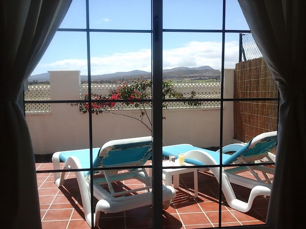 A balcony with two sun loungers and a table, overlooking a mountainous landscape.