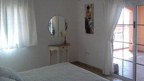 Un dormitorio con cama, un espejo redondo, una mesita y un cuadro en la pared.