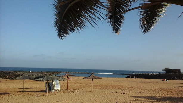 Una playa con sombrillas, sillas reclinables y un litoral rocoso.