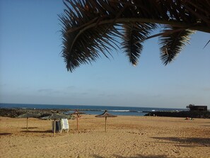 A beach with umbrellas, lounge chairs, and a rocky shoreline.