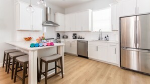 Una cocina moderna con armarios blancos, electrodomésticos de acero inoxidable y una isla central con taburetes.