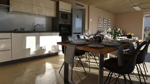A modern kitchen with built-in appliances, a dining area with a wooden table and chairs, and artwork on the walls. - Modern Villa with Pool & Sea View-40m to the Beach (Lun)