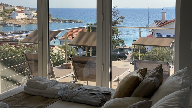 A room with a large window overlooking a coastal area, including a marina and buildings. There is a bed with pillows and a folded towel on it. - Modern Villa with Pool & Sea View-40m to the Beach (Lun)