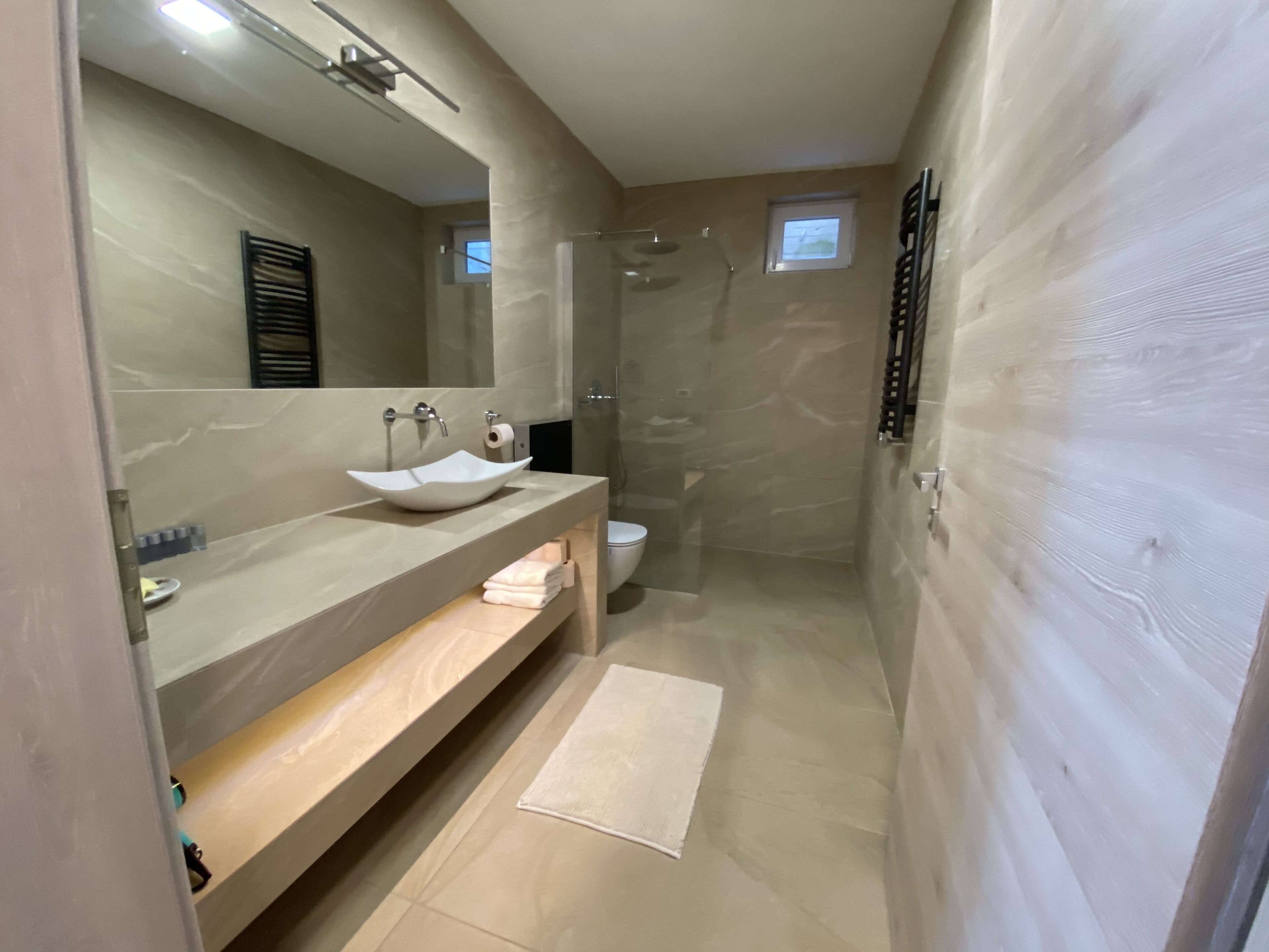 A modern bathroom with a large mirror, a beige sink, a toilet, and a glass-enclosed shower.