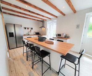 A modern kitchen with a wooden island, black bar stools, a stainless steel refrigerator, and a microwave.