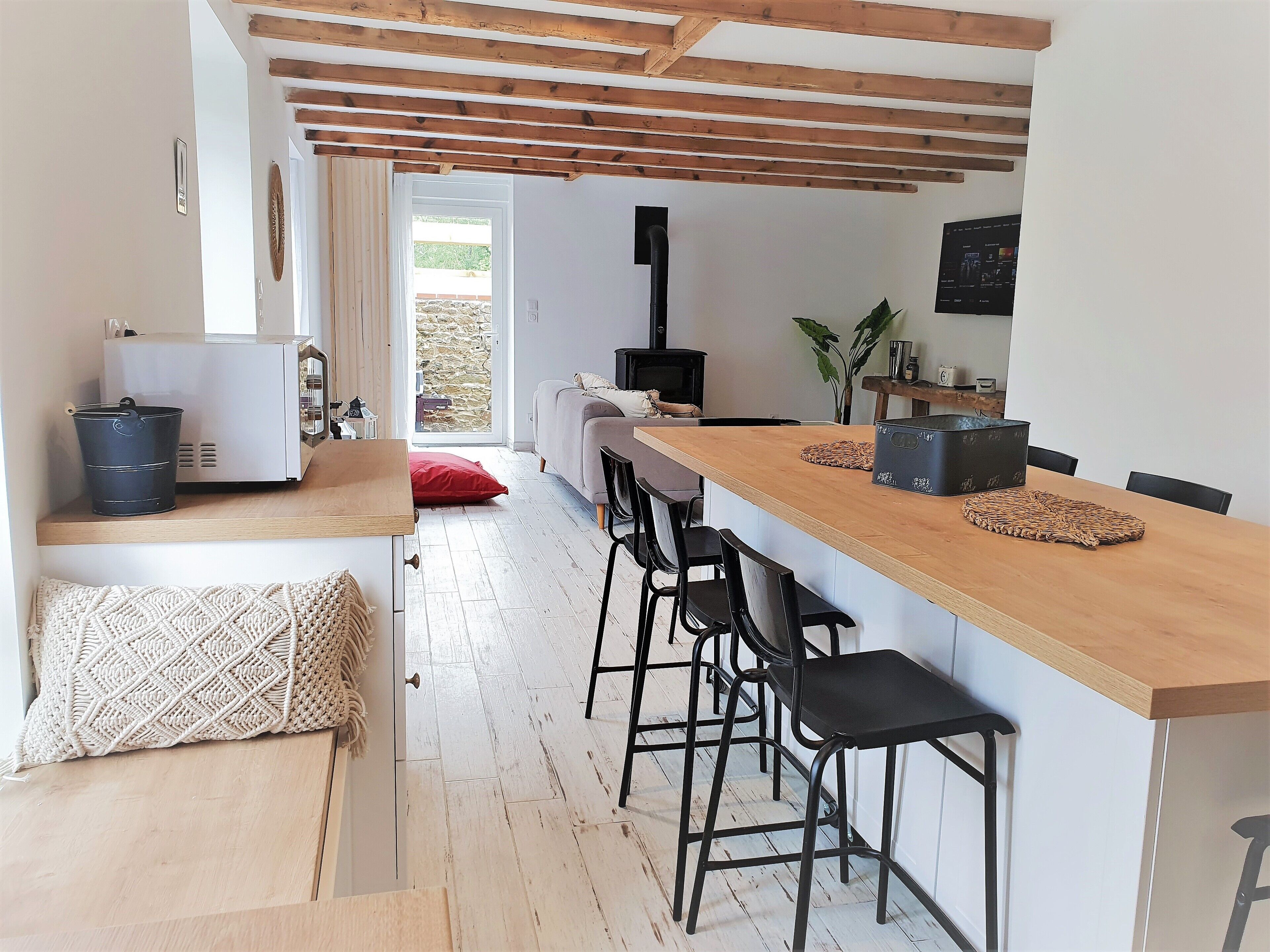 Une cuisine moderne avec un bar en bois, des chaises noires et un mur en pierre.