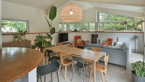Un vaste espace de vie comprenant une table à manger en bois, un canapé gris et une grande fenêtre donnant sur un paysage verdoyant.