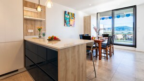 Une cuisine moderne dotée d’un îlot central, de luminaires suspendus et d’un coin repas offrant une vue sur la ville.