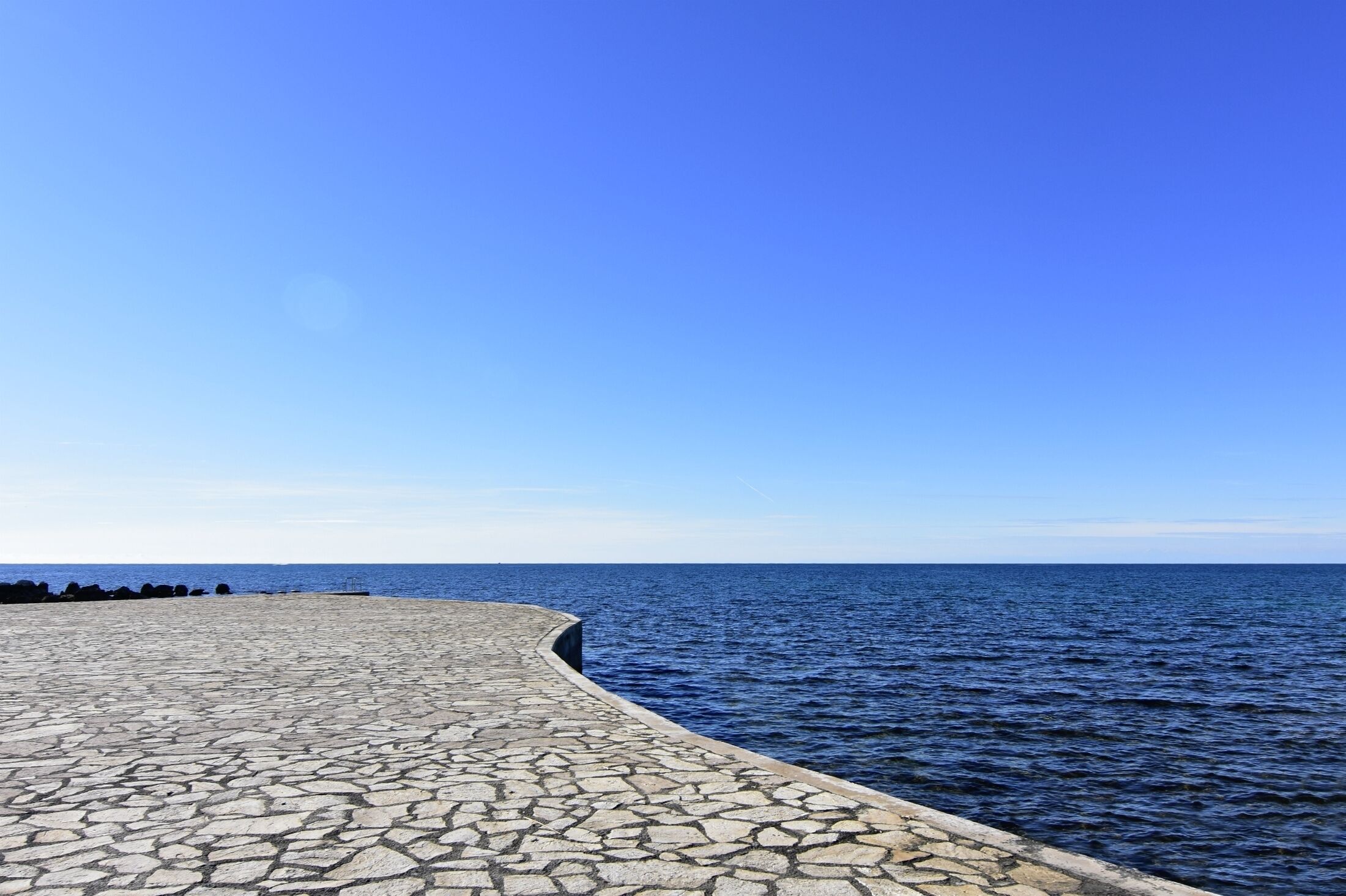 Una passeggiata lungomare lastricata in pietra con vista libera sul mare sotto un cielo azzurro.