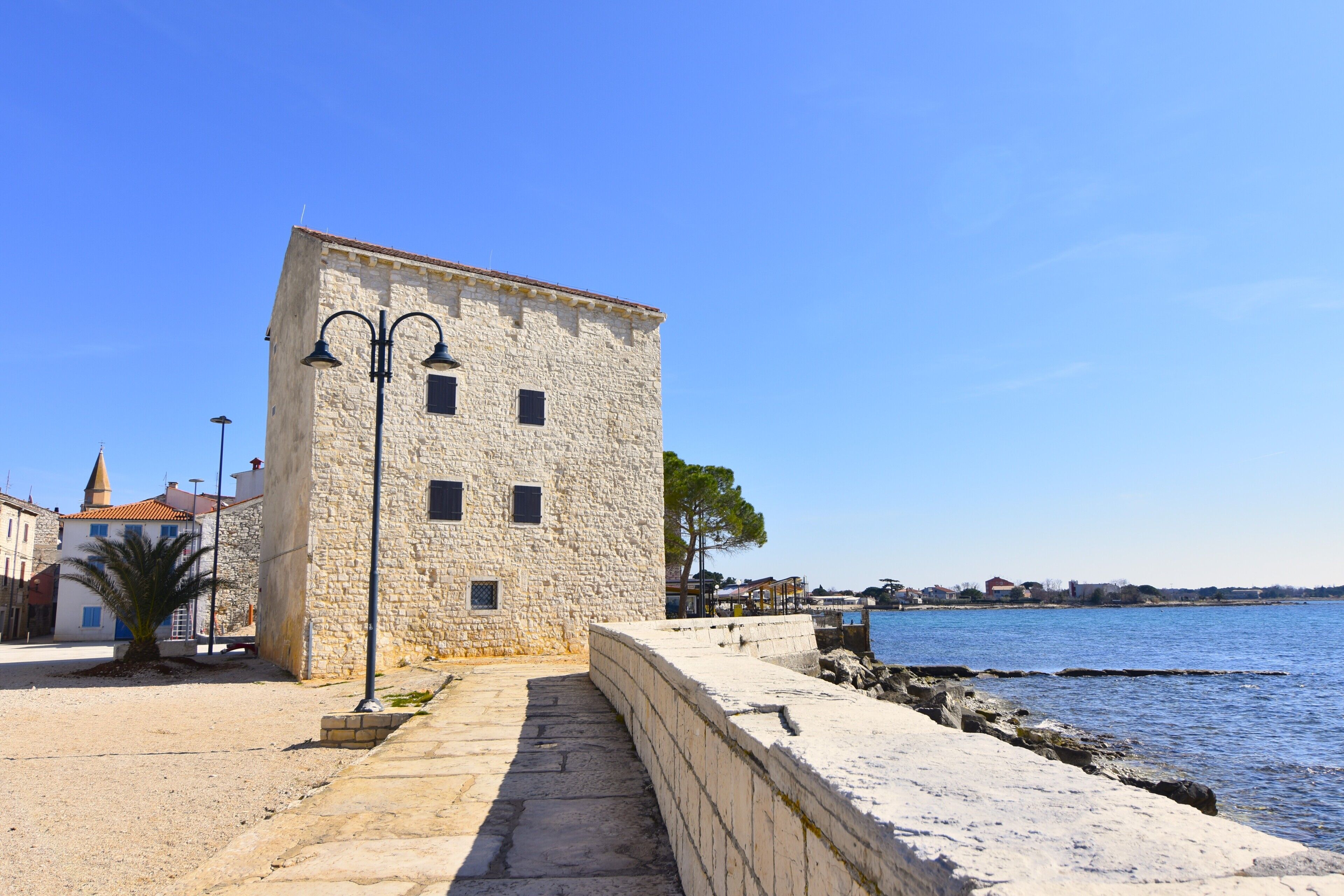 A stone building with a portico and a view of the sea.