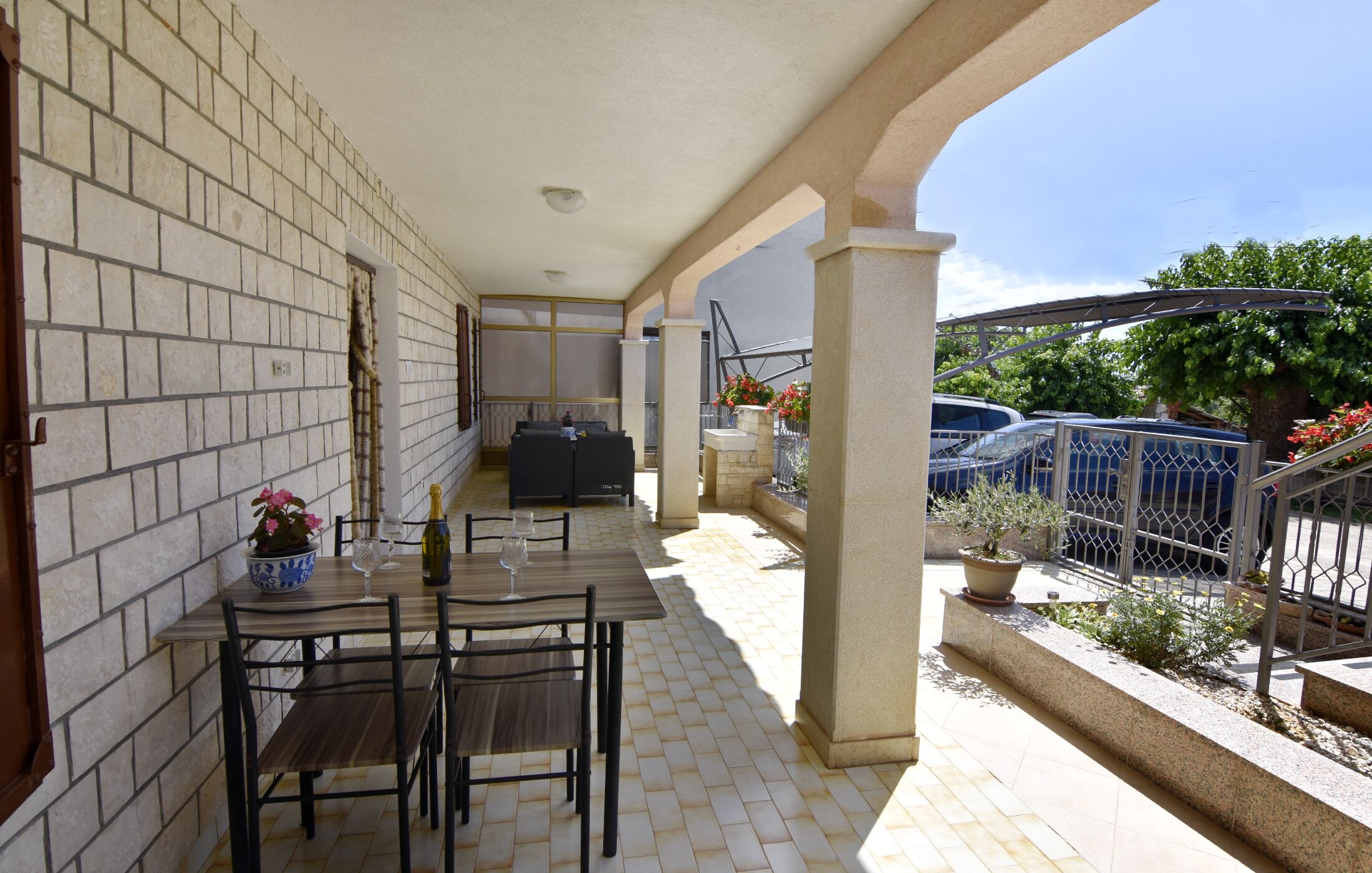 A covered outdoor patio with a table set for two, a sofa, and a potted plant.