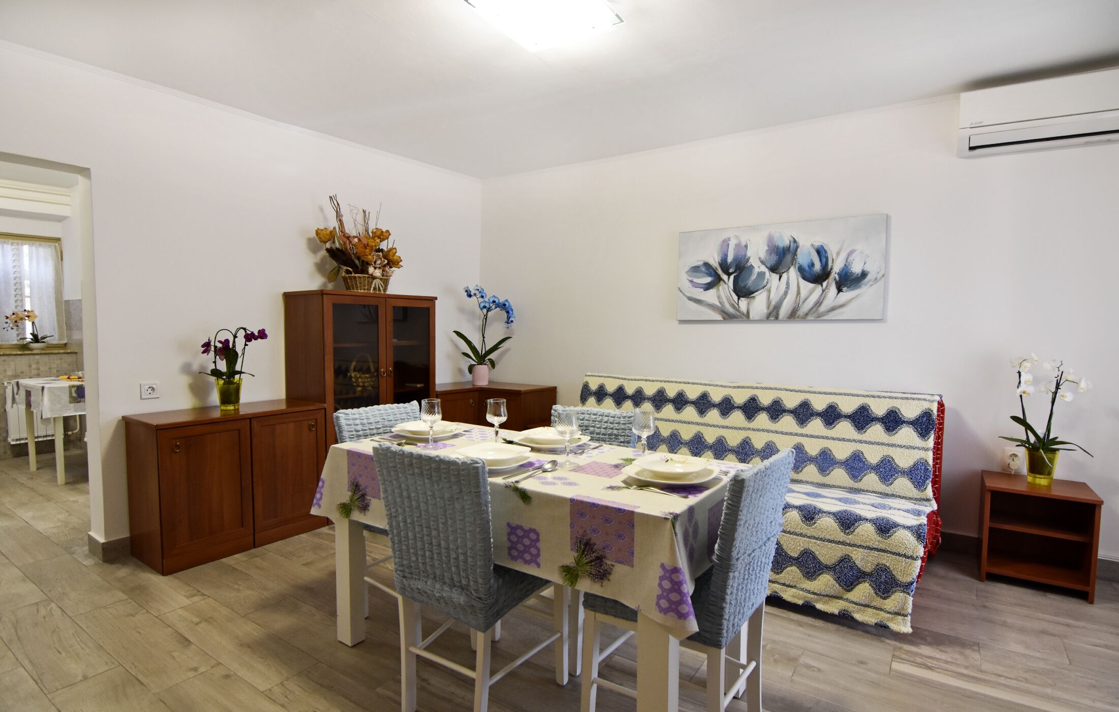 Un coin repas avec une table dressée pour quatre personnes, un canapé et un meuble orné de fleurs.