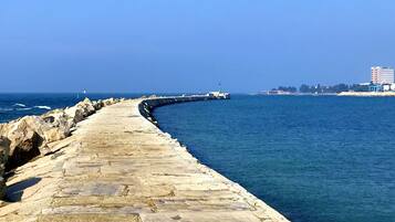 A stone pier extending into the sea with a lighthouse in the distance.