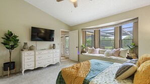Een slaapkamer met een bed, een dressoir, een televisie en een raam met uitzicht op groen.