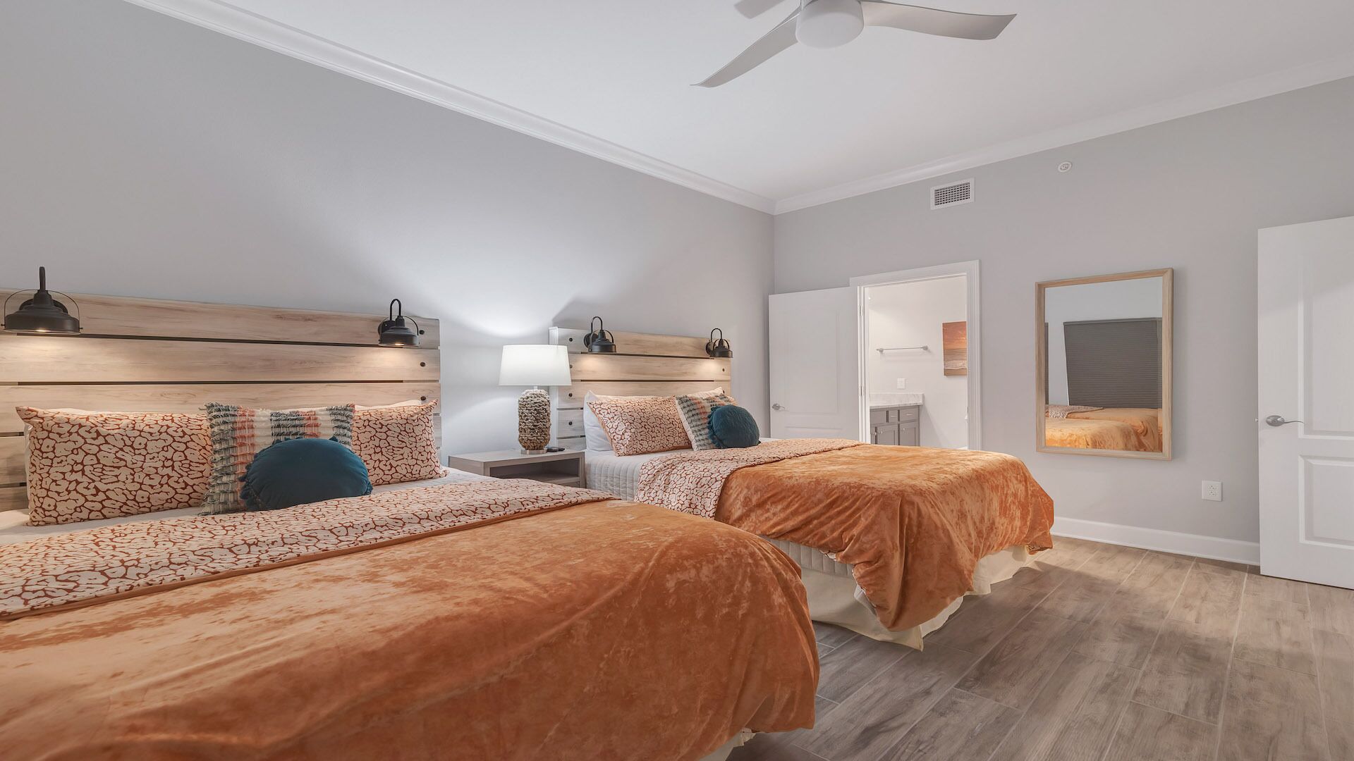 A modern bedroom with two beds, a ceiling fan, and a large mirror.