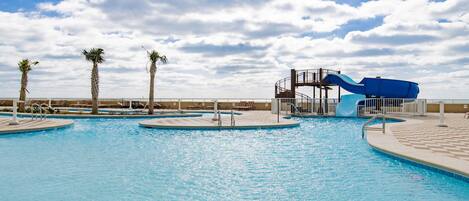 A swimming pool with a water slide, palm trees, and a clear sky.