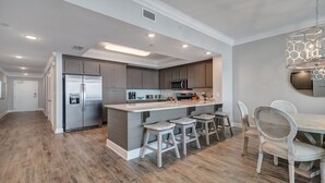 A modern kitchen with a central island, bar stools, and a dining table with chairs. - New Complex! Lazy River/Slide! Penthouse Level! (Orange Beach)