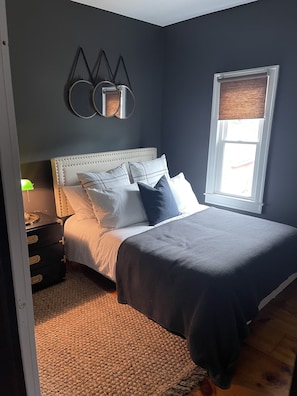Une chambre à coucher avec un lit, une table de chevet, une lampe, une fenêtre et un élément décoratif mural.
