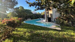 A swimming pool surrounded by lush greenery and a covered patio area.