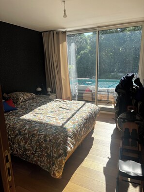 Un dormitorio con cama, una silla, una mesa y vistas a una piscina al aire libre.