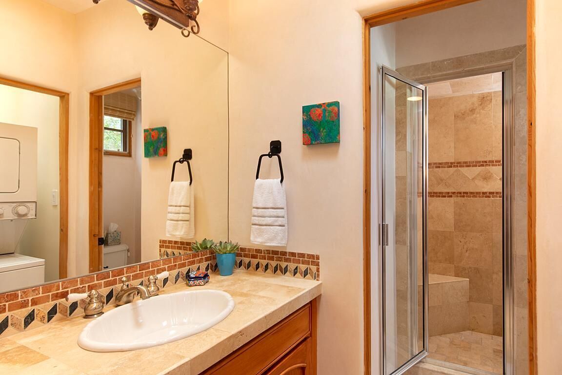 A bathroom with a large mirror, a sink, a shower, and decorative tiles.