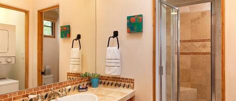 A bathroom with a large mirror, a sink, a shower, and decorative tiles.