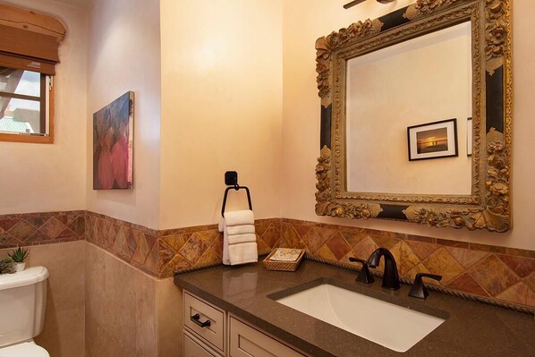 A bathroom with a large ornate mirror, a white sink, a towel rack, and a painting on the wall.