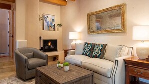 Un salon avec une cheminée, un canapé, un fauteuil, une table basse et une lampe.