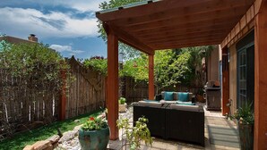 Une terrasse couverte avec des meubles d’extérieur, une clôture en bois et des plantes en pot.